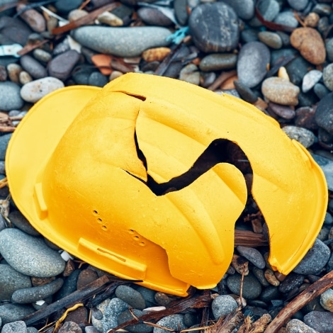 Cracked work helmet on the floor covered with pebble stones