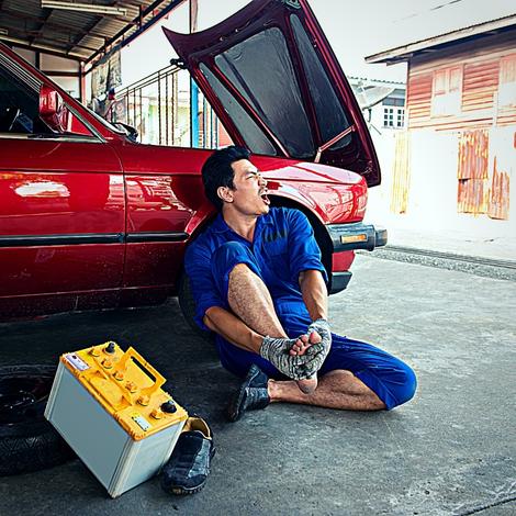 Asian mechanic get Injury and suffering at foot from battery car in garage. Concept of providing a secondary injury in workers' comp