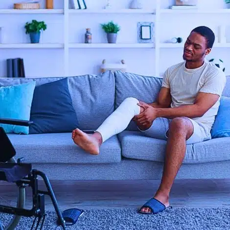 Young black guy with injured leg sitting on sofa.