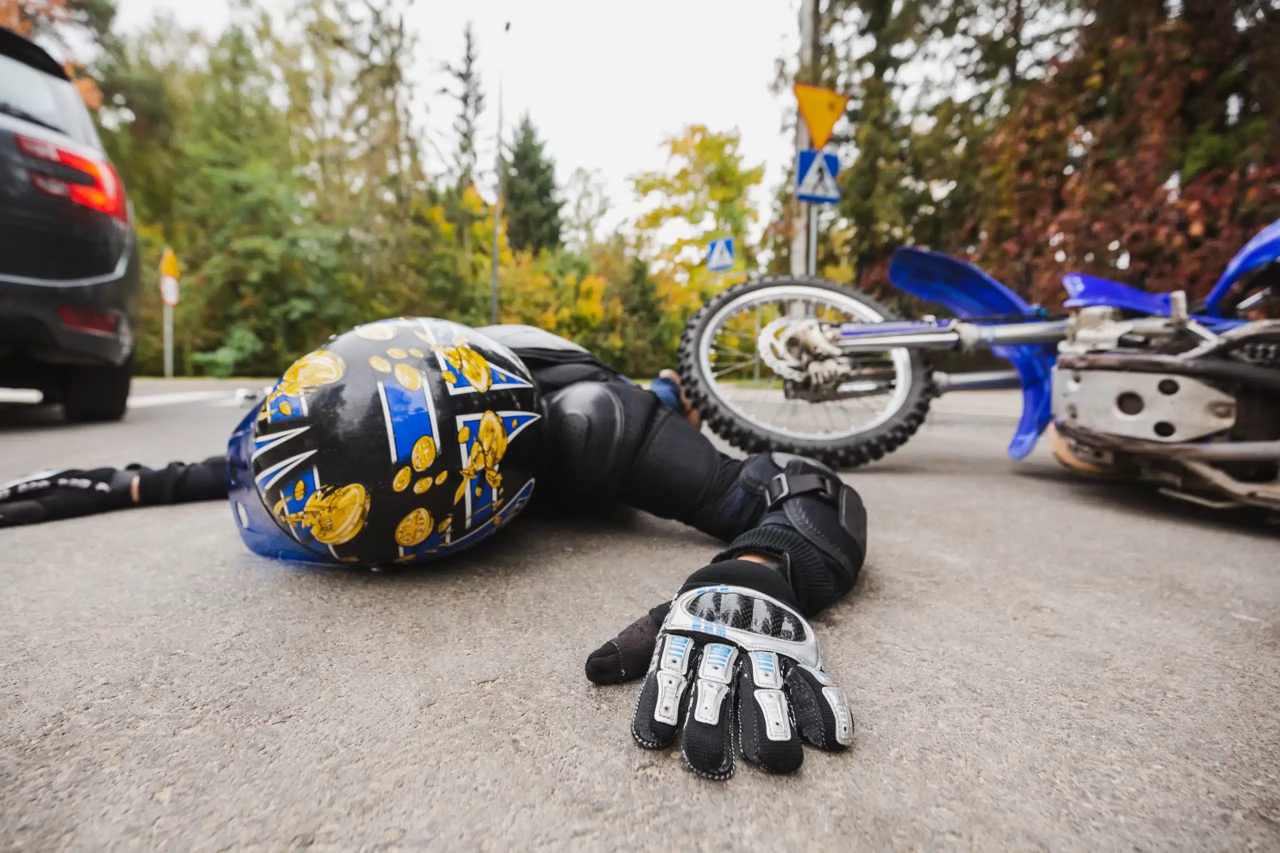 Injured motorcyclist lying on road beside fallen blue bike