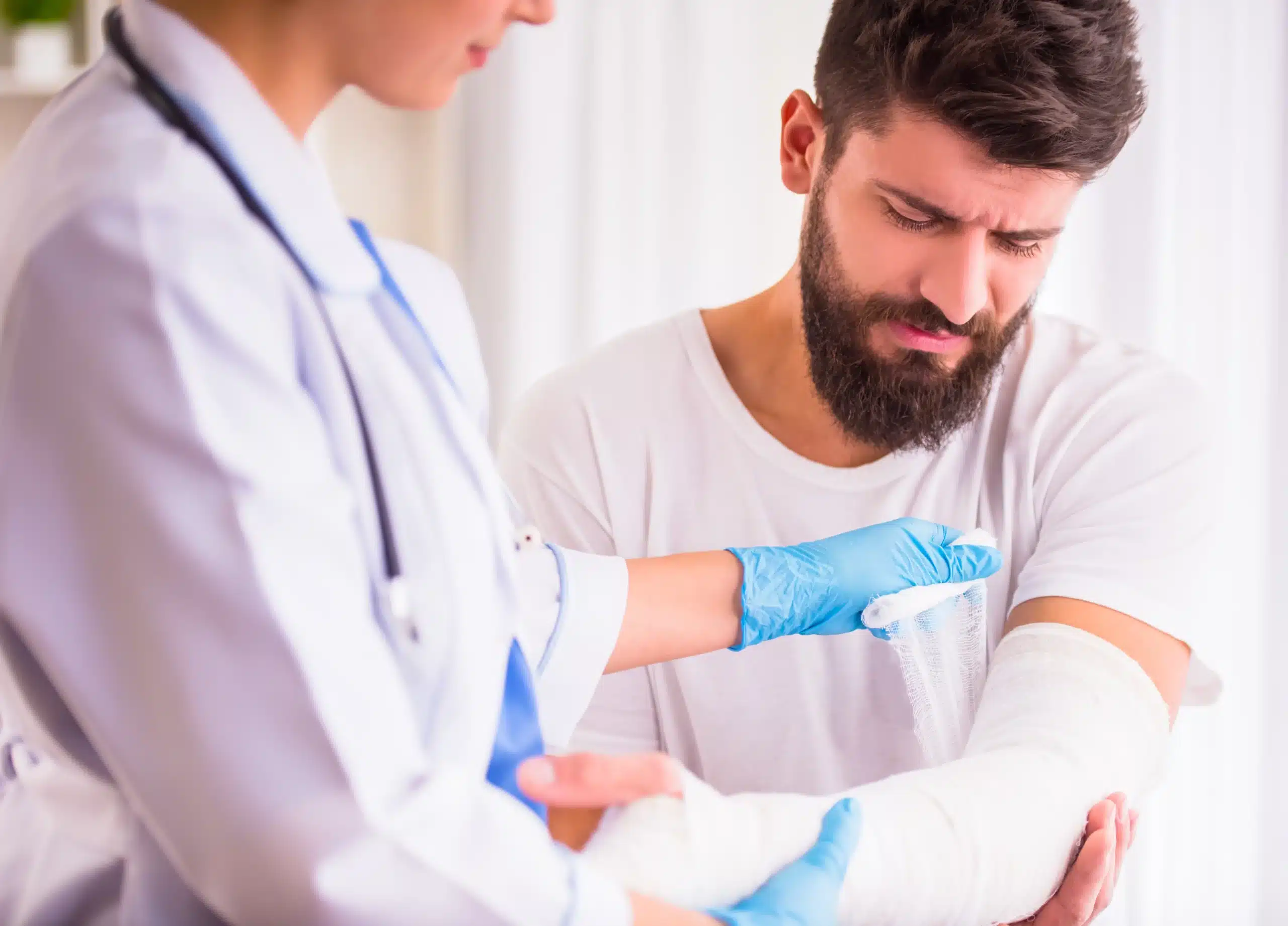 Doctor bandaging injured worker’s arm with blue gloves