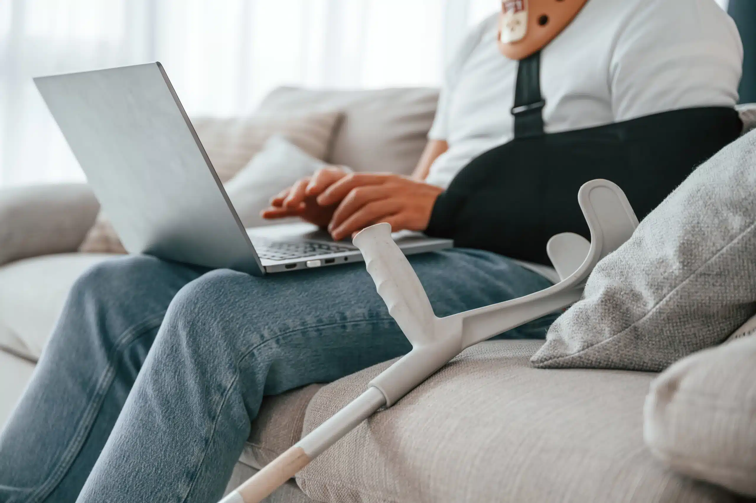 Person in neck brace and arm sling using laptop on couch