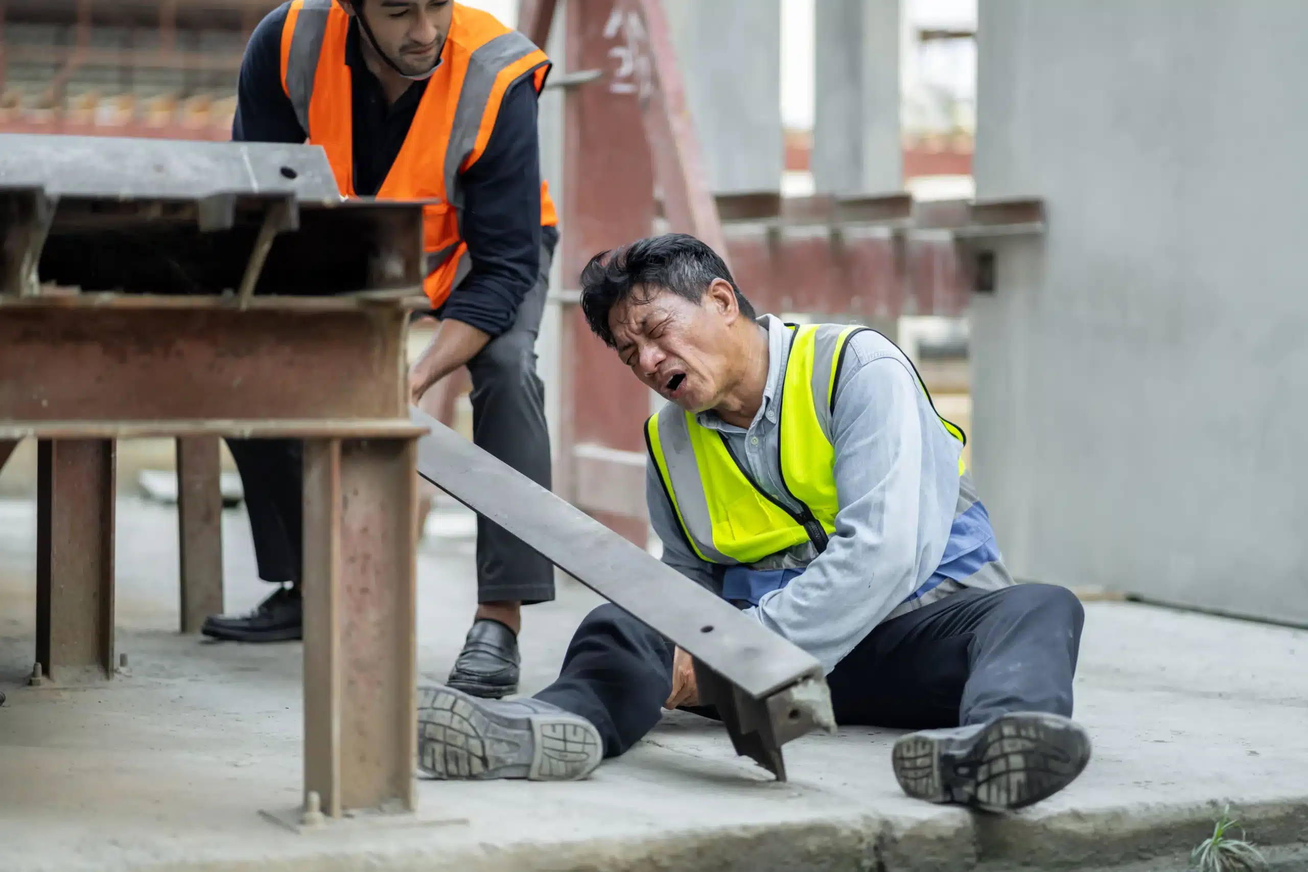 Injured construction worker clutching knee receives help from coworker in safety vest