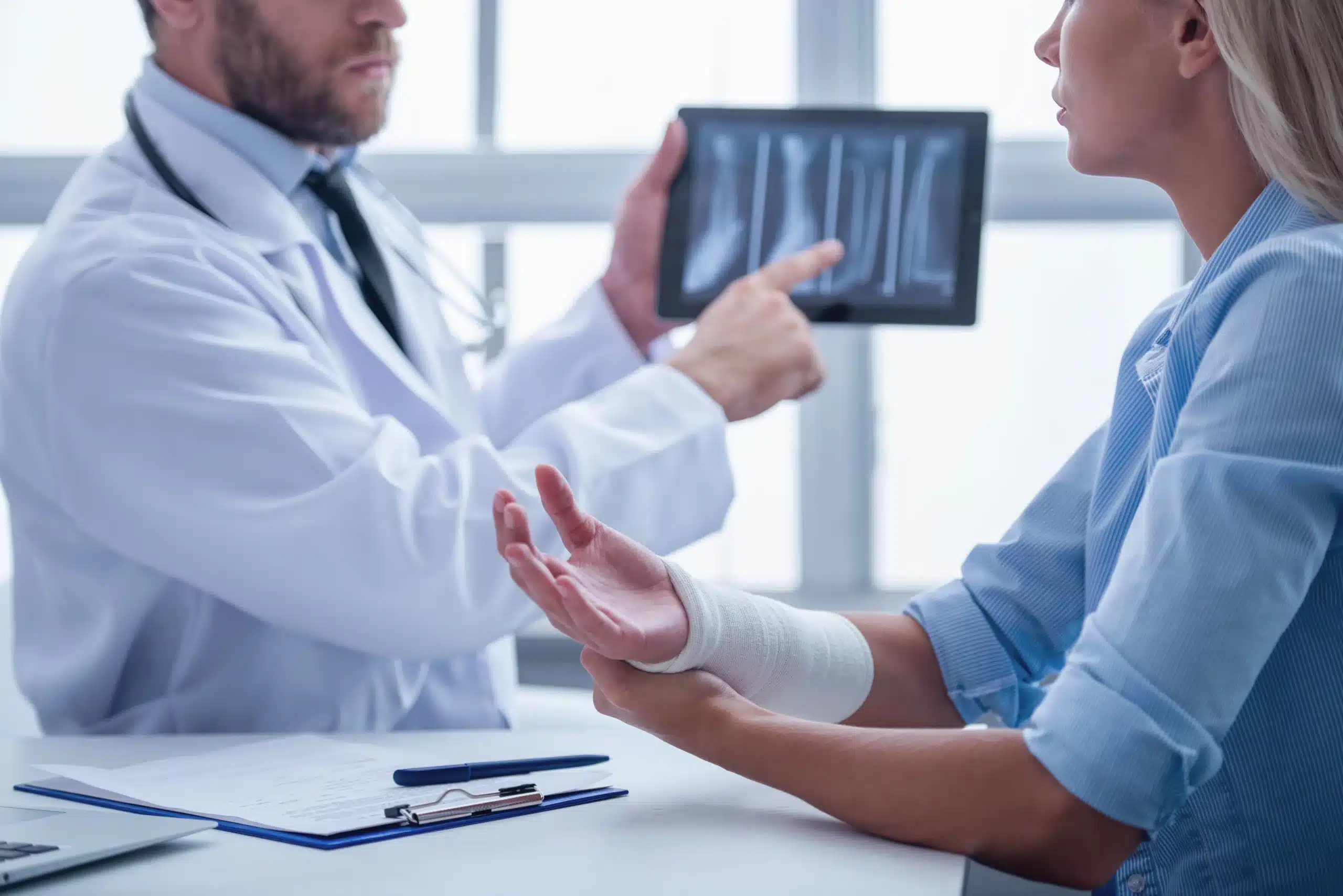 Doctor shows X-ray on tablet to injured patient with bandaged arm