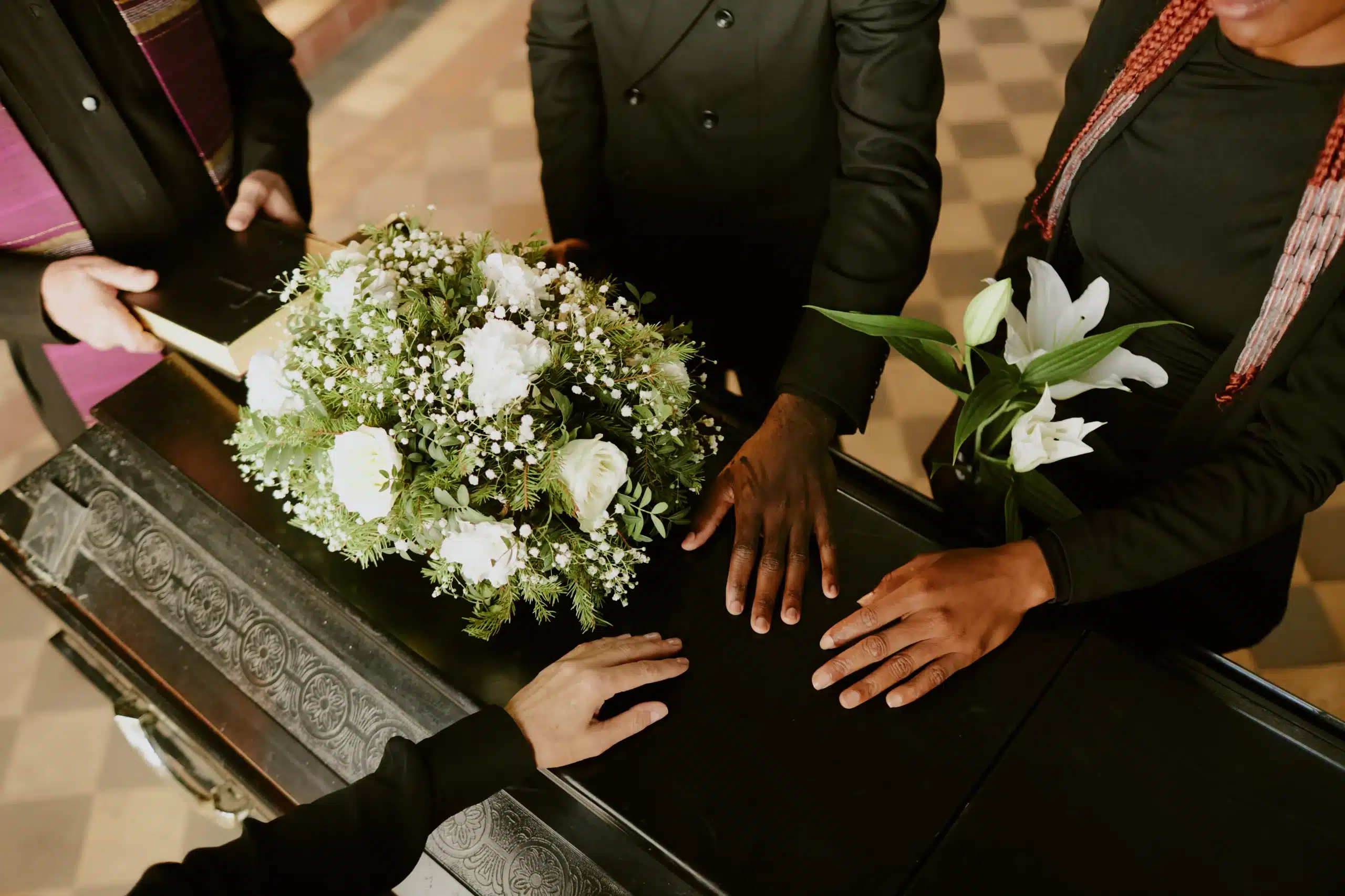 Mourners' hands on a black casket with white flowers, symbolizing the grief and legal implications of wrongful death in Illinois.
