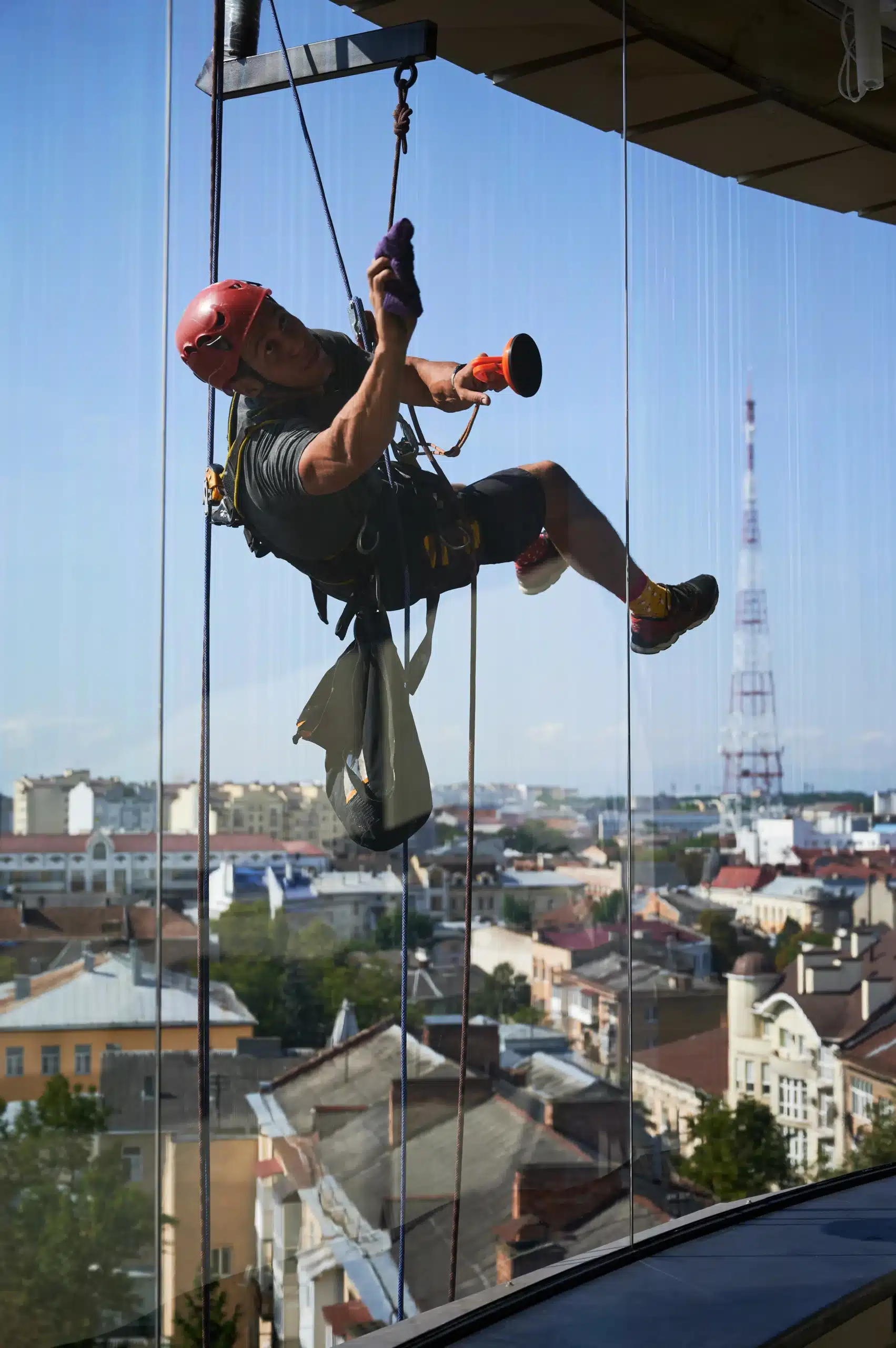 Window washer in red helmet suspended high above city cleaning glass, illustrating unsafe working conditions and employer liability in Illinois.